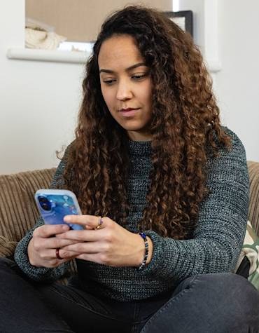 Woman looking at her phone on a sofa, used by Ecotricity to illustrate its app