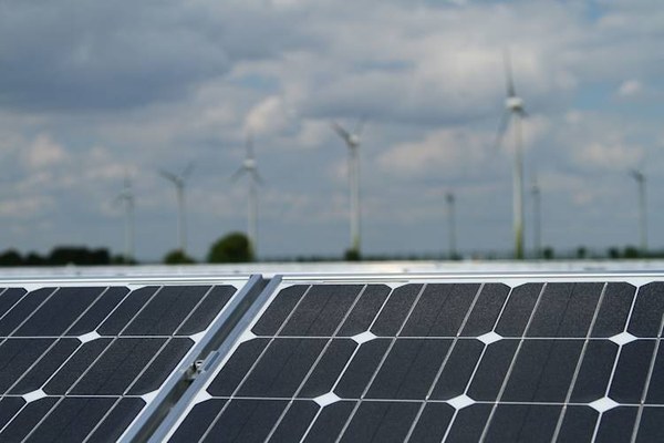 Solar panels in the foreground with wind turbines on the horizon under a cloudy sky