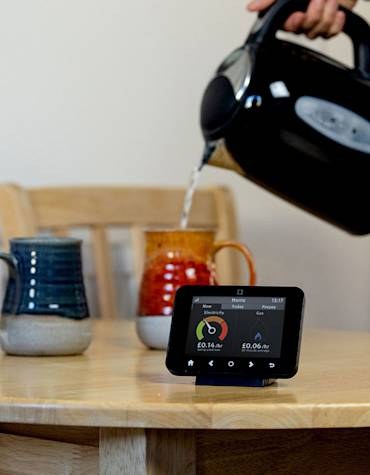 Smart meter in-home display on a kitchen table while a kettle is being poured