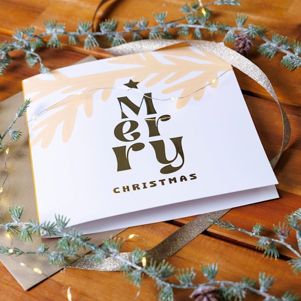 Luxe witte kerstkaart met Merry Christmas in goudkleurige folie op een houten tafel