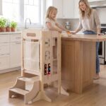Bambina in piedi su una torre Montessori in legno accanto al piano cucina insieme alla mamma
