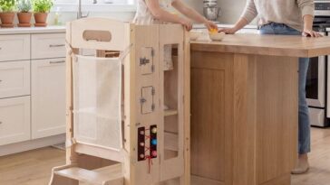 Bambina in piedi su una torre Montessori in legno accanto al piano cucina insieme alla mamma