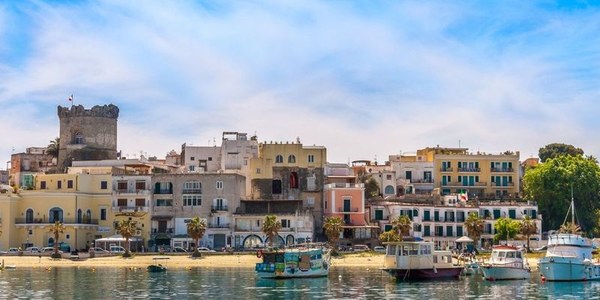 Porto di Forio a Ischia con case chiare, barche ormeggiate e una torre sullo sfondo