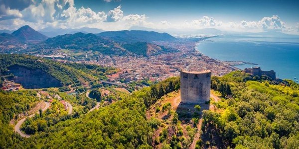 Veduta dall'alto della costa vicino a Salerno con una torre tra le colline verdi, immagine Ferryhopper per i traghetti di Salerno